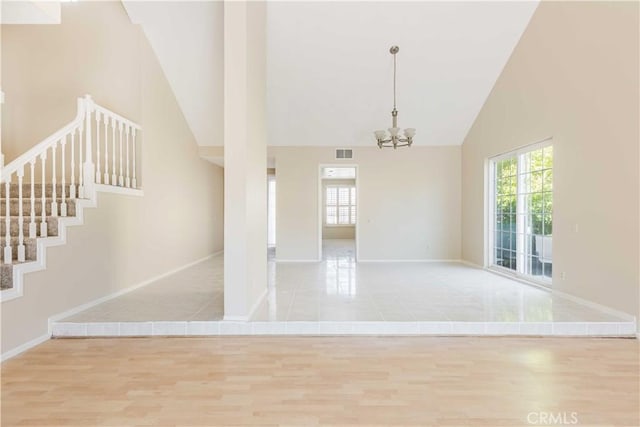 unfurnished room with wood finished floors, visible vents, high vaulted ceiling, stairs, and a chandelier