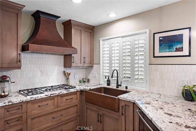 kitchen featuring light stone counters, stainless steel appliances, a sink, custom range hood, and backsplash