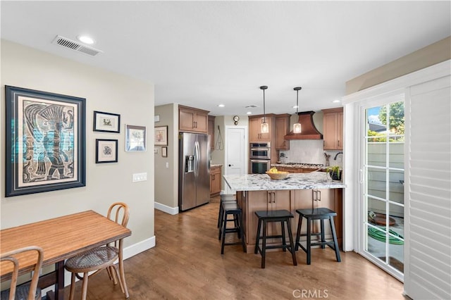 kitchen with visible vents, custom range hood, backsplash, appliances with stainless steel finishes, and a peninsula