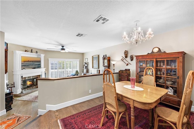 dining area with visible vents, a textured ceiling, a glass covered fireplace, and wood finished floors