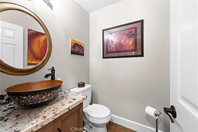 bathroom with toilet, vanity, baseboards, and wood finished floors