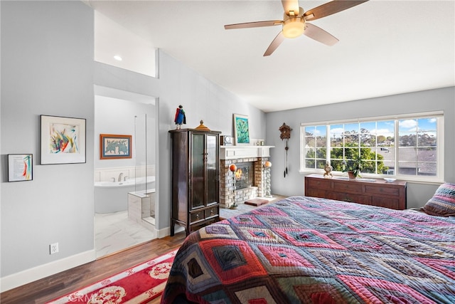 bedroom with wood finished floors, baseboards, ensuite bath, lofted ceiling, and a brick fireplace