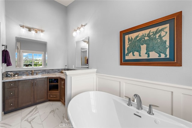 full bathroom with a wainscoted wall, marble finish floor, a decorative wall, a soaking tub, and vanity