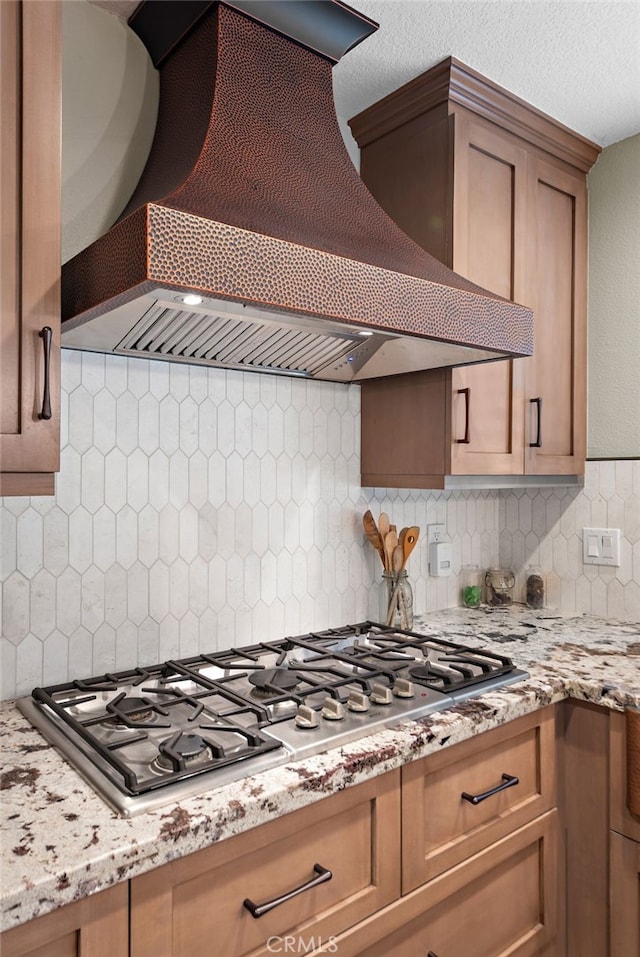 kitchen featuring decorative backsplash, light stone countertops, premium range hood, and stainless steel gas cooktop