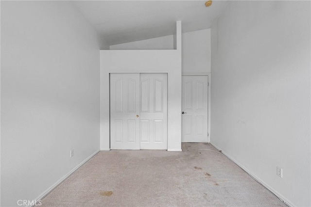 unfurnished bedroom with lofted ceiling, carpet flooring, baseboards, and a closet