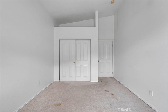 unfurnished bedroom with a closet, baseboards, lofted ceiling, and carpet floors