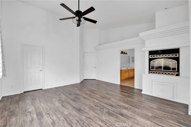 unfurnished living room with high vaulted ceiling, wood finished floors, baseboards, and ceiling fan