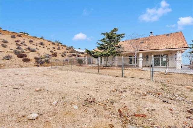 rear view of house featuring a gate, fence, a chimney, stucco siding, and a tile roof