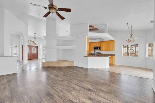 unfurnished living room with arched walkways, light wood-style flooring, ceiling fan with notable chandelier, and a sink