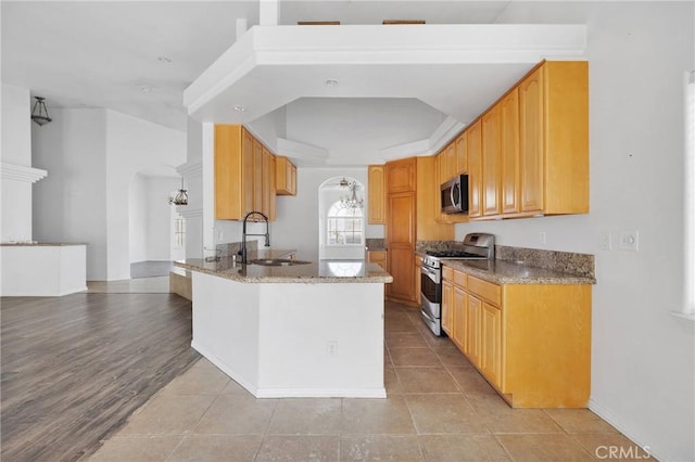 kitchen featuring a sink, stainless steel appliances, arched walkways, and light stone counters