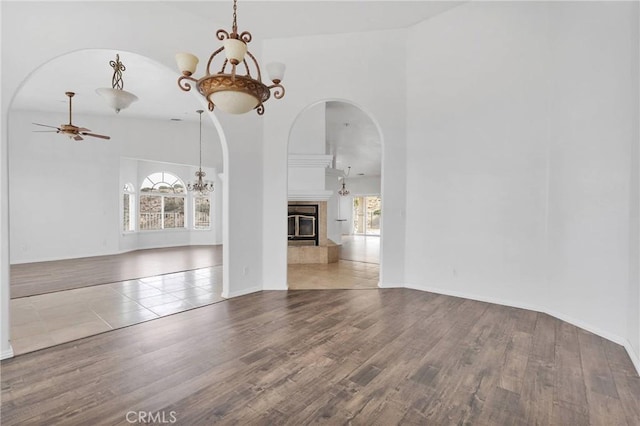 unfurnished dining area with arched walkways, ceiling fan with notable chandelier, a high ceiling, and wood finished floors