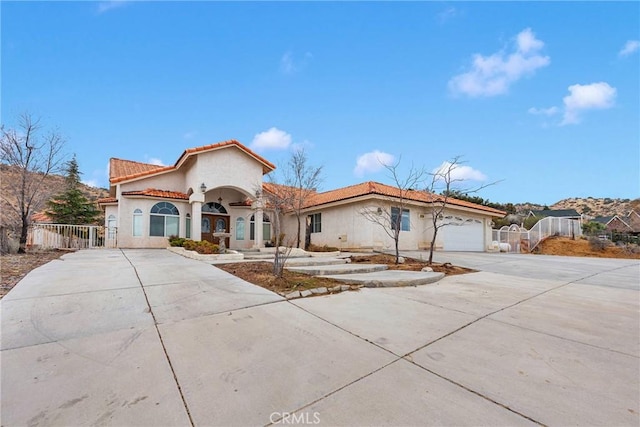 mediterranean / spanish home with fence, stucco siding, concrete driveway, a garage, and a tiled roof