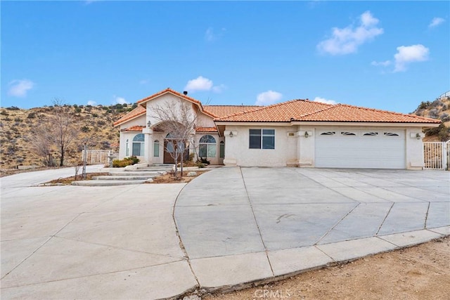 mediterranean / spanish-style house with a tiled roof, a garage, stucco siding, fence, and driveway
