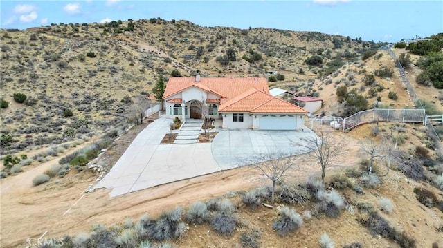 mediterranean / spanish home with a tile roof, a desert view, concrete driveway, fence, and a garage