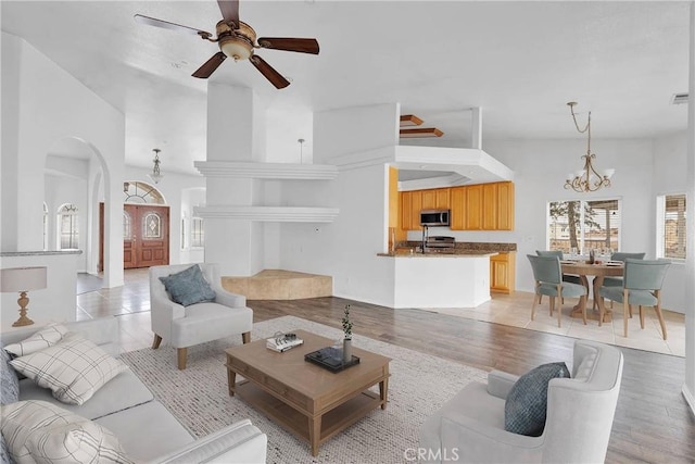 living area with ceiling fan with notable chandelier, vaulted ceiling, arched walkways, and light wood-style floors