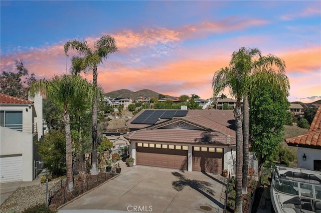 view of front of home with driveway, a tile roof, roof mounted solar panels, a mountain view, and an attached garage