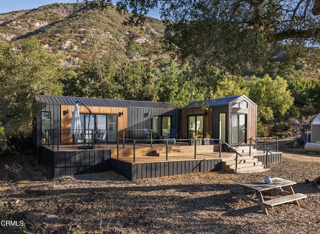 back of house with a standing seam roof, a deck with mountain view, and metal roof