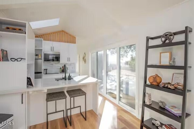 kitchen with open shelves, vaulted ceiling with skylight, a sink, light wood-style floors, and white cabinetry