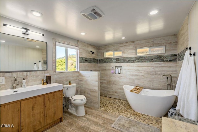 bathroom featuring visible vents, toilet, a freestanding bath, walk in shower, and vanity