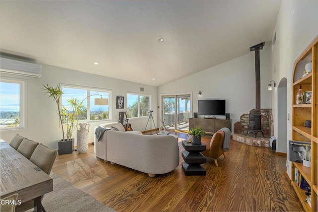 living room featuring vaulted ceiling, wood finished floors, a wood stove, and a wall mounted AC