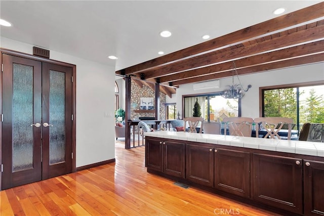 kitchen featuring beam ceiling, open floor plan, french doors, light wood-style floors, and dark brown cabinets