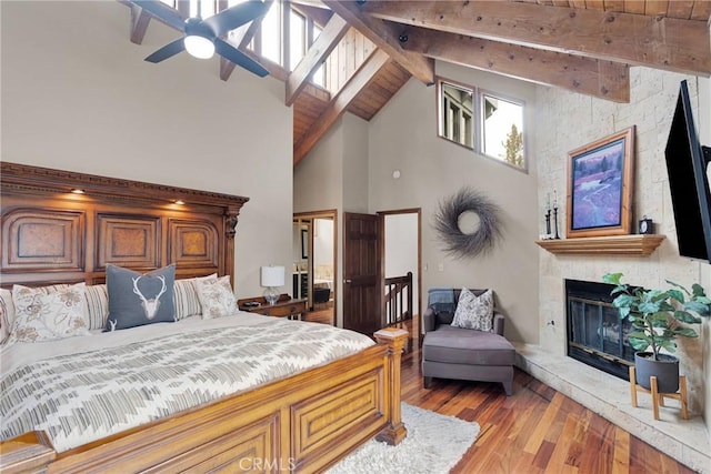 bedroom featuring beamed ceiling, a large fireplace, light wood-style floors, and high vaulted ceiling