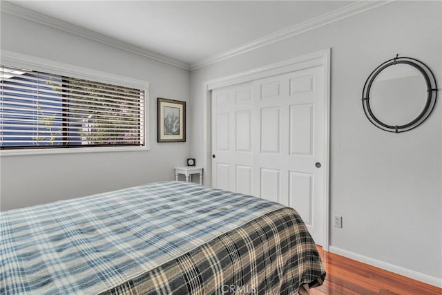 bedroom featuring a closet, ornamental molding, baseboards, and wood finished floors