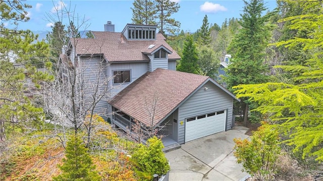 view of front of home featuring an attached garage, a chimney, driveway, and a shingled roof