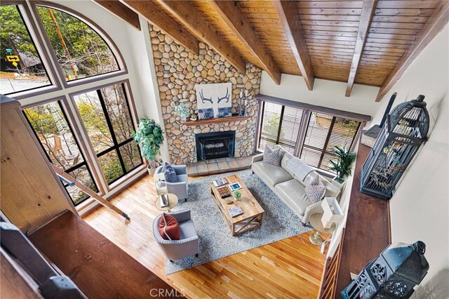 living area with beam ceiling, high vaulted ceiling, wood finished floors, a stone fireplace, and wood ceiling