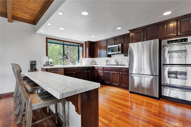 kitchen with a warming drawer, backsplash, dark brown cabinetry, appliances with stainless steel finishes, and a peninsula