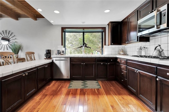 kitchen featuring a sink, backsplash, appliances with stainless steel finishes, and light wood finished floors