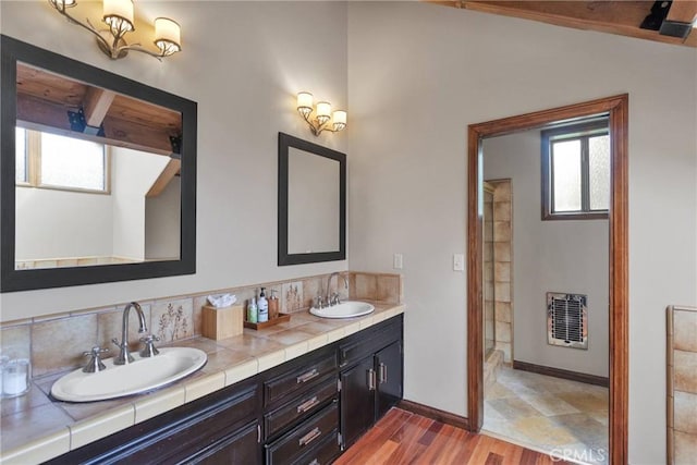 full bathroom with double vanity, heating unit, wood finished floors, and a sink