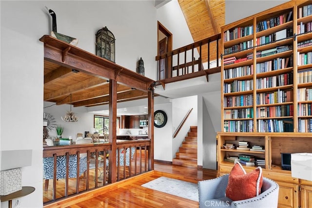 living area featuring beamed ceiling, wood finished floors, a high ceiling, wooden ceiling, and stairs