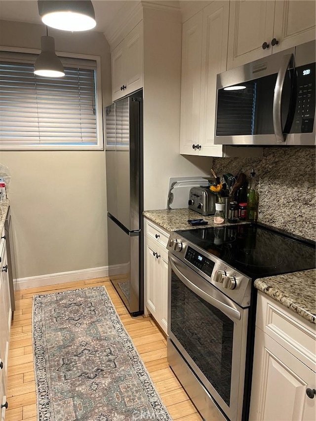 kitchen with backsplash, light stone counters, appliances with stainless steel finishes, light wood-style floors, and white cabinets