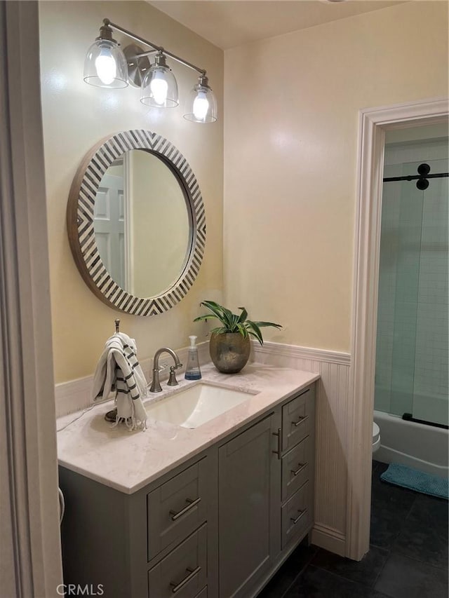 bathroom with tile patterned flooring, a wainscoted wall, toilet, shower / bath combination with glass door, and vanity