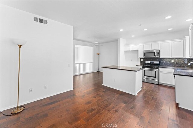 kitchen featuring dark wood-style floors, a sink, appliances with stainless steel finishes, dark countertops, and tasteful backsplash