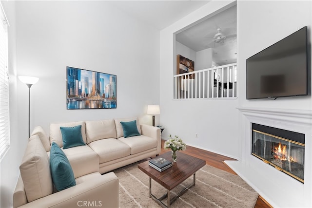 living room featuring a glass covered fireplace, wood finished floors, baseboards, and a ceiling fan