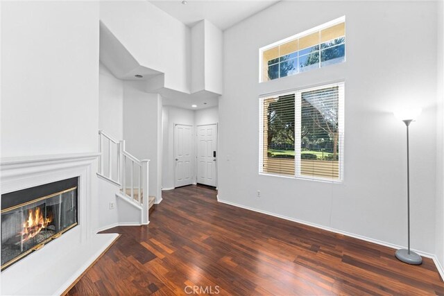 unfurnished living room featuring a glass covered fireplace, a towering ceiling, baseboards, and wood finished floors