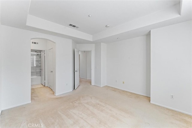 empty room with visible vents, a raised ceiling, arched walkways, carpet floors, and baseboards