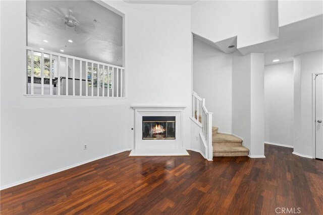 unfurnished living room with wood finished floors, a glass covered fireplace, recessed lighting, stairway, and baseboards