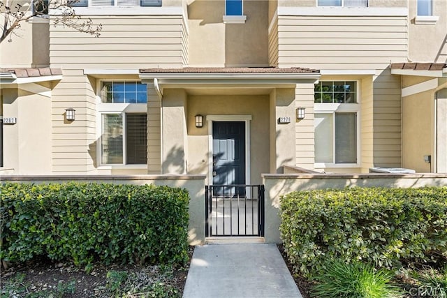 doorway to property featuring a tiled roof, stucco siding, and a gate