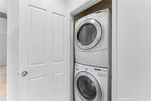 laundry room featuring laundry area, stacked washer and clothes dryer, visible vents, and a textured wall