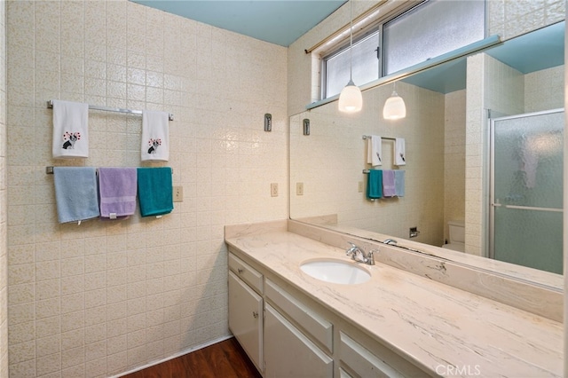 bathroom featuring toilet, a stall shower, wood finished floors, tile walls, and vanity