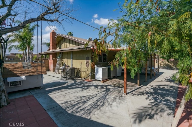 back of property with central air condition unit, stucco siding, a chimney, and a patio area