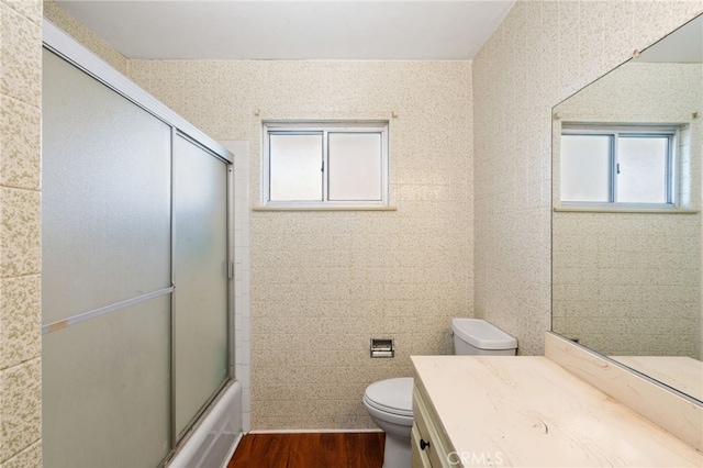 bathroom with vanity, toilet, wood finished floors, and enclosed tub / shower combo