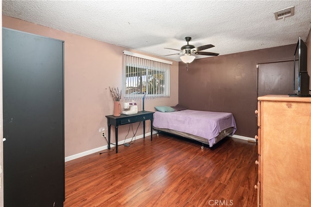 bedroom with visible vents, baseboards, wood finished floors, a textured ceiling, and a ceiling fan