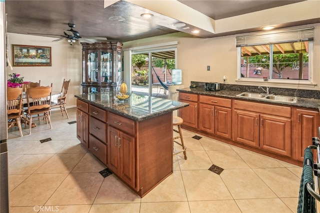 kitchen with a breakfast bar area, light tile patterned floors, a sink, brown cabinets, and a center island