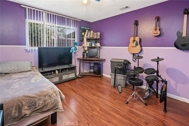 bedroom with a ceiling fan, baseboards, wood finished floors, visible vents, and a textured ceiling