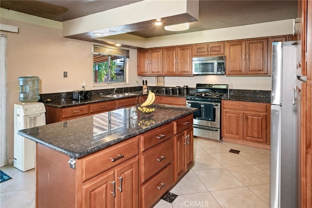 kitchen with light tile patterned flooring, a sink, stainless steel appliances, brown cabinets, and a center island