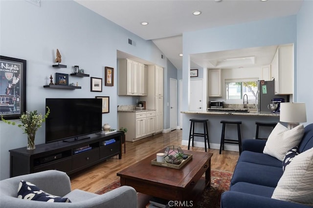 living room with visible vents, baseboards, recessed lighting, light wood-style flooring, and a raised ceiling